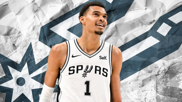 a picture of victor wembanyama smiling infront of the spurs logo